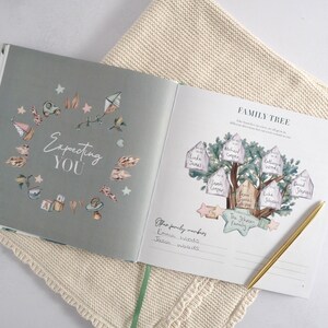 May include: A light blue and green baby memory book with a watercolor illustration of a family tree on the right page. The text "FAMILY TREE" is at the top of the page. The left page has a circle of baby-themed illustrations with the text "Expecting YOU" in the center.