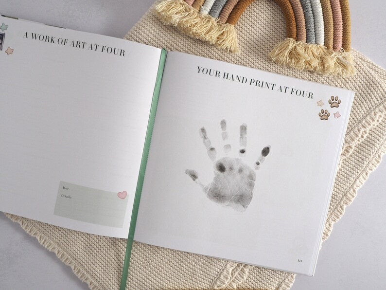 May include: A white book with the text "A work of art at four" and "Your hand print at four" on the cover. The book has a green spine and a handprint on the right page. There are small star and paw print stickers on the page.
