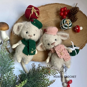 Puede incluir: Dos juguetes de ratón de crochet con bufandas y sombreros verdes y rosas. Los juguetes están sentados en una rodaja de madera con bayas rojas, una piña y un adorno verde y dorado.