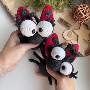 Puede incluir: Dos criaturas hechas a mano con ganchillo, con grandes ojos blancos, cuerpos negros y alas rojas y negras. Las criaturas se sostienen sobre un fondo neutro. El texto "MONTY'S CROCHET" es visible en una peque&ntilde;a etiqueta.