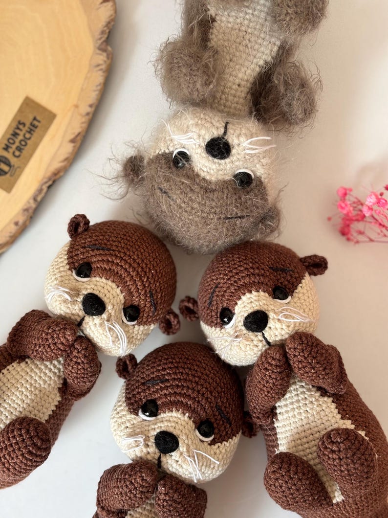 Pode incluir: Lontras de croch&ecirc; feitas &agrave; m&atilde;o em tons de castanho e creme. As lontras t&ecirc;m olhos pretos e bigodes brancos. A imagem mostra v&aacute;rias lontras em v&aacute;rias poses, mostrando os detalhes do design artesanal. O logotipo "MONYS CROCHET" &eacute; vis&iacute;vel.