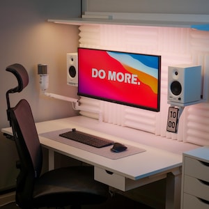 Puede incluir: Un escritorio blanco con una silla de oficina negra, un monitor de computadora que muestra el texto "DO MORE." y un teclado y un ratón. Hay paneles acústicos blancos en la pared detrás del escritorio.