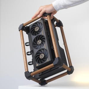 Puede incluir: Una tarjeta gráfica ASUS GeForce RTX negra con tres ventiladores de refrigeración, encerrada en un marco rectangular hecho de cuatro varillas de madera conectadas por juntas de esquina negras. La tarjeta tiene detalles dorados.