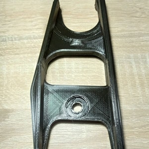 Puede incluir: Una pieza de pl&aacute;stico negro impresa en 3D con un agujero en el centro y dos ranuras en la parte superior.