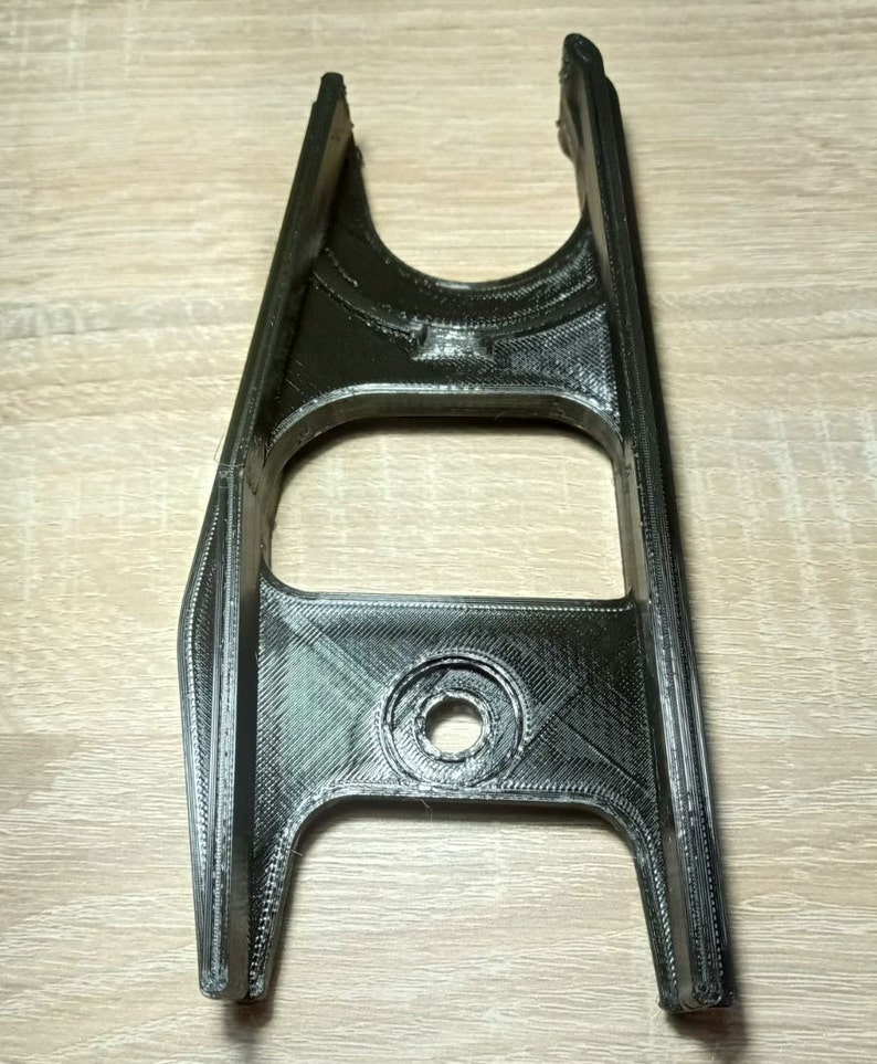 Puede incluir: Una pieza de pl&aacute;stico negro impresa en 3D con un agujero en el centro y dos ranuras en la parte superior.