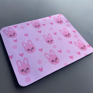 May include: A pink mouse mat with a repeating pattern of pink bunnies with angry expressions and pink hearts.