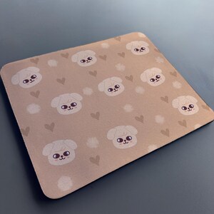 May include: A brown mouse mat with a repeating pattern of white cartoon dogs with brown eyes and pink noses. The background is a light brown with small white and brown hearts.