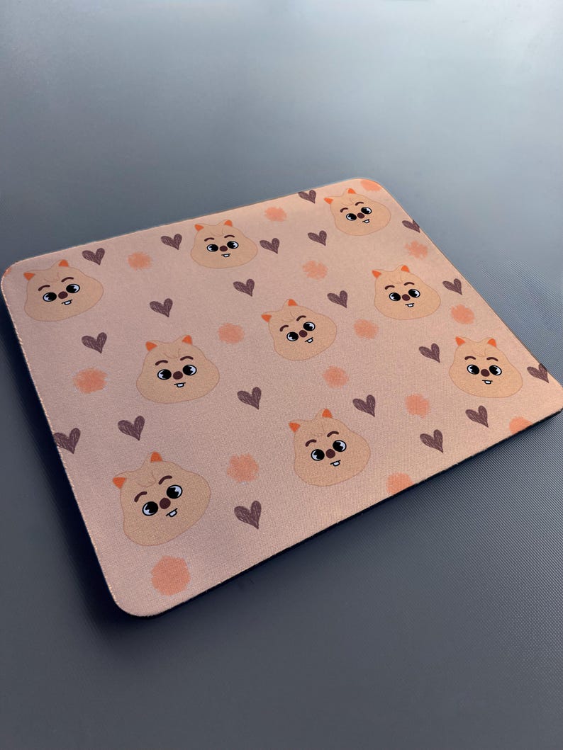 May include: A pink mouse mat with a repeating pattern of cartoon animals with brown eyes and hearts. The animals are light brown with orange accents.