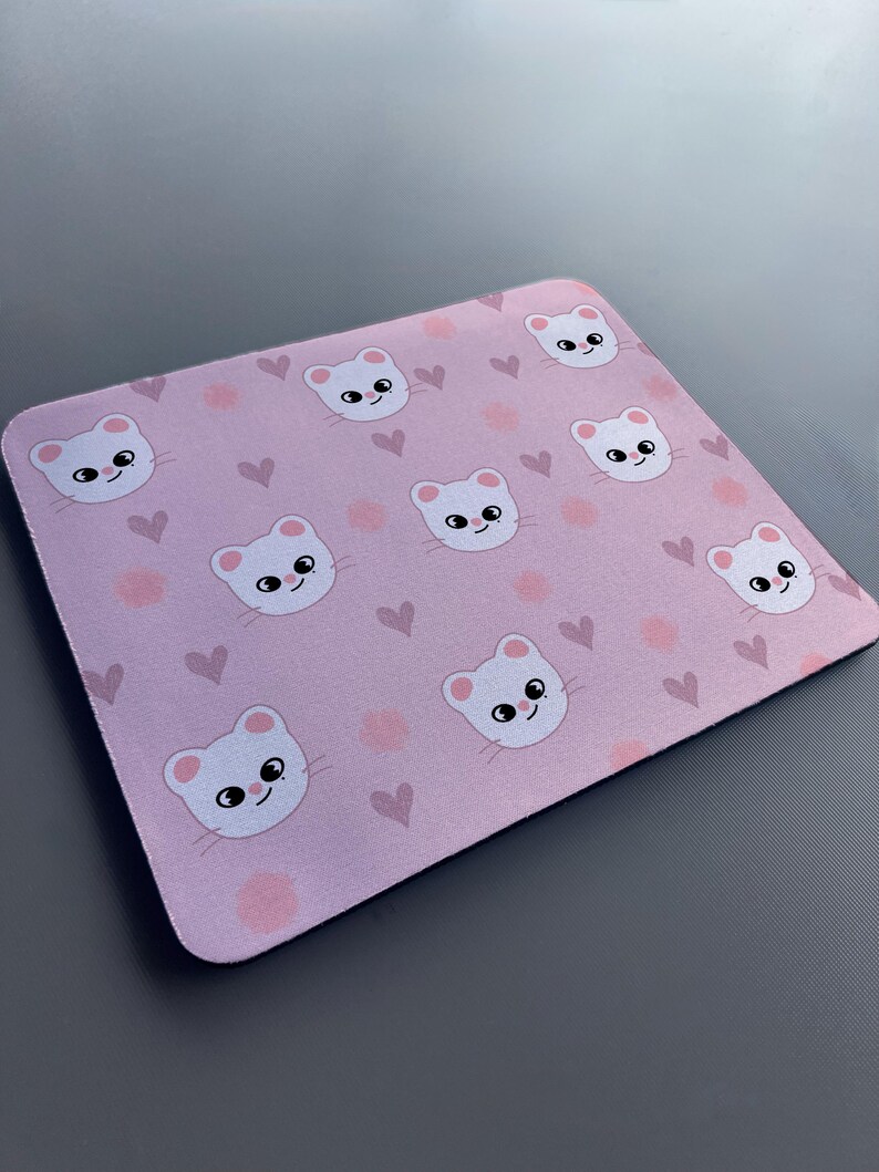 May include: A pink mouse mat with a repeating pattern of white cartoon cats and pink hearts.