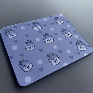 May include: A blue mouse mat with a repeating pattern of a cartoon animal with hearts and white dots.