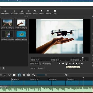May include: A computer screen displaying the Shotcut video editing software interface. The workspace includes a playlist panel with multiple image thumbnails, a central preview window showing a drone, and a timeline with audio tracks.