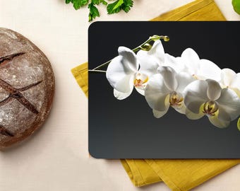 Könnte beinhalten: Ein schwarzes Schneidebrett mit einer weißen Orchideenblüte darauf. Das Schneidebrett ist von verschiedenen Lebensmitteln umgeben, darunter ein Brotlaib, Tomaten, eine Limette und ein Stück Käse.