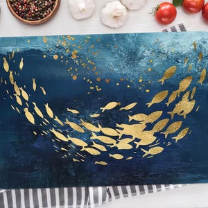 May include: A blue and gold kitchen placemat with a design of a school of fish swimming in a circle. The fish are gold and the background is a dark blue with gold flecks.