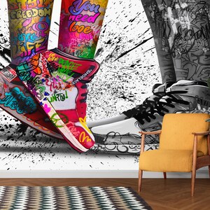 May include: A pair of sneakers with colorful graffiti designs, including the words "freedom", "you need love", and "unify". The sneakers are set against a black and white splatter paint background.