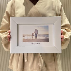 May include: A white rectangular photo frame displaying a photograph of a person and child walking on a beach. The image has a warm colour palette. The words "Love you loads" are printed in a script font at the bottom of the photo.