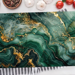 Pode incluir: Uma tábua de corte retangular com um design de mármore verde e dourado. A tábua tem um acabamento brilhante e está sobre uma toalha listrada. Tomates, alho e especiarias circundam a tábua.