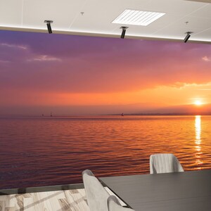 May include: A scenic sunset over a calm body of water with a few sailboats in the distance. The sky is a vibrant mix of orange, pink, and purple hues, reflecting on the water's surface.