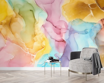 May include: Abstract wall art featuring a colourful, swirling pattern of pink, yellow, blue, and green hues with gold accents. The art is displayed on a wall with a grey armchair and a small table in front of it.