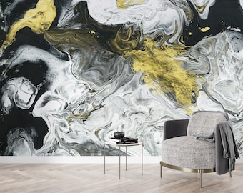 May include: Abstract wall art featuring a swirling pattern of black, white, and gold paint. The art is displayed in a living room setting with a grey armchair and a small round table.