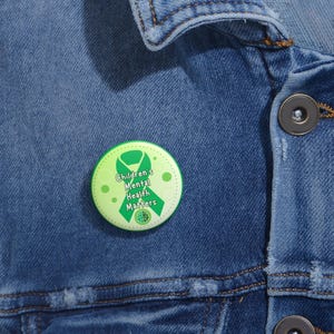 May include: Green button with a green ribbon and the text "Children's Mental Health Matters" on a light blue denim jacket.