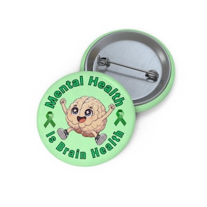 May include: A light green button with the text "Mental Health Is Brain Health" encircling a cartoon brain character. The brain has a smiling face and is jumping with its arms raised. Two green ribbons are on either side of the brain.