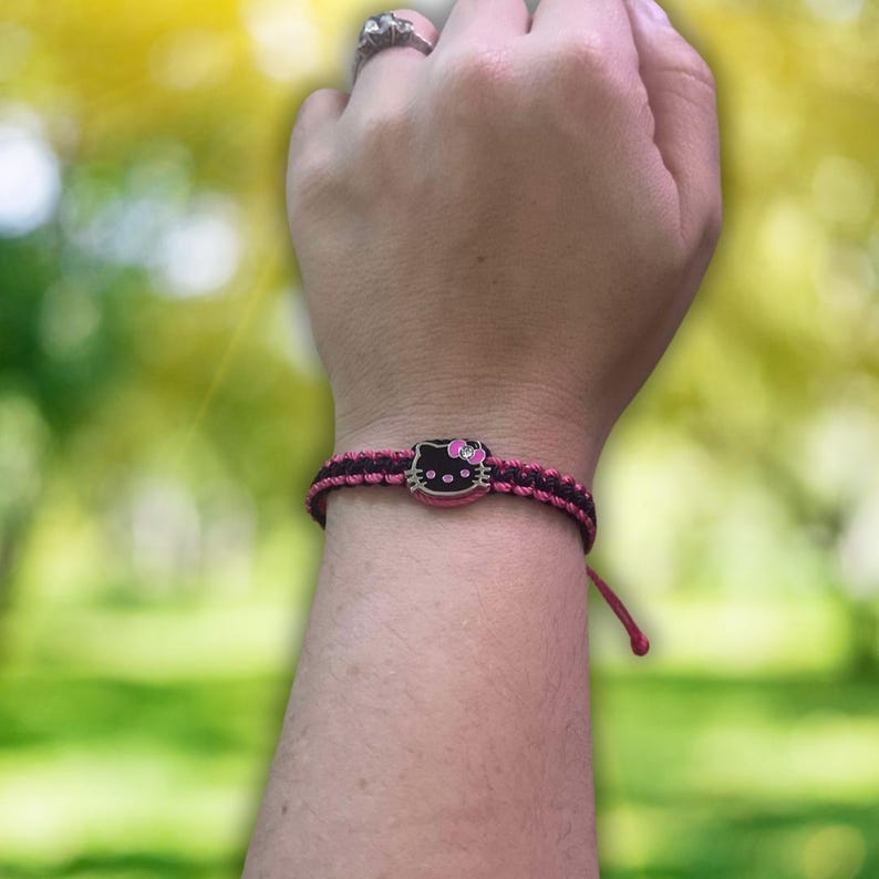 Pode incluir: Um bracelete de amizade preto e rosa com um amuleto Hello Kitty. O bracelete &eacute; feito de corda tran&ccedil;ada e tem um esquema de cores rosa e preto.