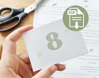 May include: A hand holds a white card with a large number 8 in light green, accompanied by two small star illustrations. A PDF icon is visible. Scissors and other printed cards are in the background, suggesting a craft or DIY project.