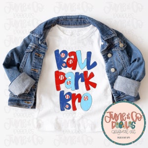 May include: White t-shirt with a red, blue, and light blue graphic that says "Ball Park Bro" with baseballs on each letter.