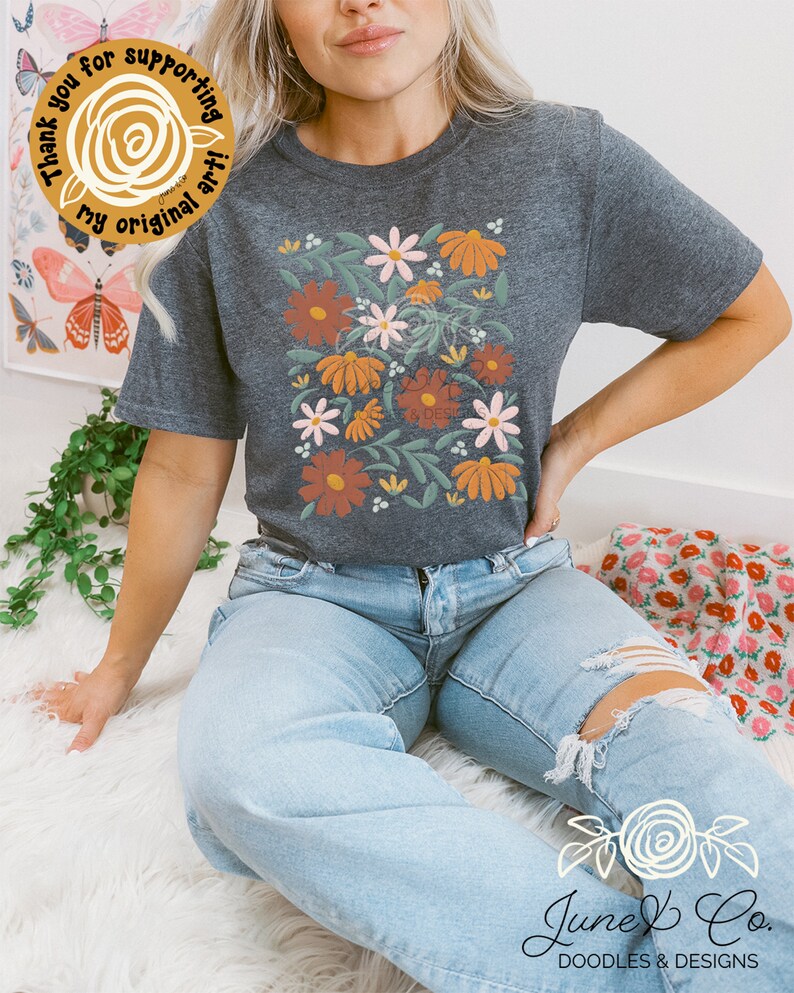May include: A dark gray t-shirt with a floral design featuring orange, pink, and white flowers on a green leafy background. The text "Thank you for supporting my original art!" is on a yellow circle sticker.