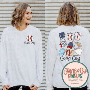 May include: White sweatshirt with a baseball graphic and the text "Game Day" on the front. The back of the sweatshirt features a baseball-themed design with a baseball, bat, glove, hat, cooler, hot dog, popcorn, and a folding chair. The text "Game Day" is also on the back of the sweatshirt.
