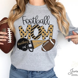 Może przedstawiać: Szara bluza z napisem "Football Mom" w czarnych i złotych literach z czarnymi i złotymi kropkami. Litery są obwiedzione czarną linią. Jest piłka nożna, kask do futbolu amerykańskiego i chorągiewka z napisem "Go team!" w kolorze czarnym i złotym.
