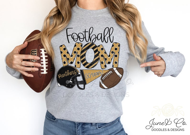 Może przedstawiać: Szara bluza z napisem "Football Mom" w czarnych i złotych literach z czarnymi i złotymi kropkami. Litery są obwiedzione czarną linią. Jest piłka nożna, kask do futbolu amerykańskiego i chorągiewka z napisem "Go team!" w kolorze czarnym i złotym.