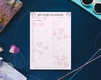 May include: A pink daily planner with a floral design and hearts. The planner has sections for today's schedule, priorities, to-do list, and mood. It also includes a section for notes.