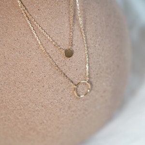 Peut inclure: Un collier en chaîne dorée avec deux pendentifs : un petit cercle et un disque plat plus grand.