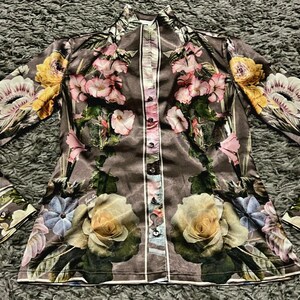 May include: A long-sleeved button-up shirt with a floral print in shades of pink, yellow, and green on a dark brown background.