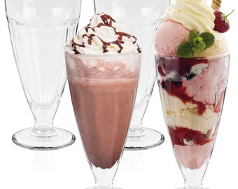 Può includere: Quattro bicchieri di milkshake in vetro trasparente con una base spessa. Un bicchiere è pieno di un milkshake al cioccolato sormontato da panna montata e sciroppo al cioccolato. Un altro bicchiere è pieno di un sundae con panna montata, gelato e bacche.