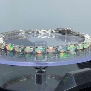 May include: A silver bracelet featuring a line of oval opals. The opals are iridescent and display a spectrum of colours.