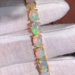 May include: A gold bracelet featuring a series of oval opals. Each opal displays a play of color with flashes of red, green, and blue. The bracelet is set on a gold band, showcasing the gemstones.