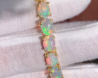 May include: A gold bracelet featuring a series of oval opals. Each opal displays a play of color with flashes of red, green, and blue. The bracelet is set on a gold band, showcasing the gemstones.