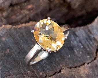 May include: A silver ring with a large, oval-shaped, yellow citrine gemstone.