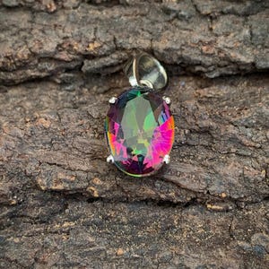 May include: A silver pendant with a large oval-shaped iridescent gemstone. The gemstone has a rainbow of colors, including red, pink, green, and blue.
