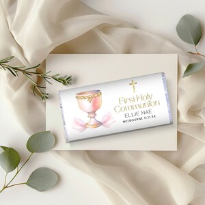 Könnte beinhalten: Weiße Schokoladentafelverpackung mit einem rosa Kelch und goldenen Akzenten. Der Text lautet "Erste Heilige Kommunion" mit dem Namen "Ellie Mae" und dem Ort "Melbourne 11.11.XX".