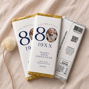 May include: Three personalized chocolate bars with gold foil wrapping. The bars feature a photo, the number 80, and text that reads "Happy 80th Johnathan." The back of one bar includes a barcode and ingredient list.