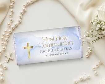 Puede incluir: Un envoltorio de chocolate blanco con un fondo de acuarela azul y una cruz dorada. El texto en el envoltorio dice "First Holy Communion Caleb Kristian Melbourne 11.11.XX".
