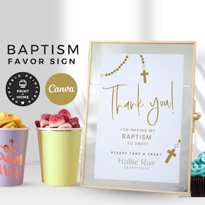 Puede incluir: Un letrero de recuerdo de bautizo con marco dorado con el texto "¡Gracias!" y "Por hacer mi bautizo tan dulce". El letrero incluye un diseño de rosario y cruz. La imagen también muestra golosinas y cupcakes coloridos.