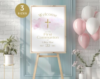 May include: A white welcome sign with a pink watercolor background and gold lettering. The sign says "Welcome to the First Communion of Lilley Mae Sat 22 Dec".