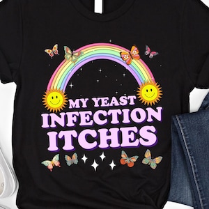 以下が含まれることがあります： 虹、蝶、ピンクの文字で「My Yeast Infection Itches」と書かれた黒いTシャツです。