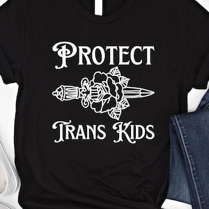 May include: Black t-shirt with white text that reads "PROTECT TRANS KIDS" and a stylised image of a dagger with a rose.