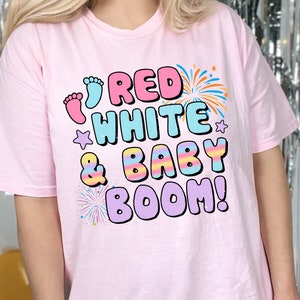 May include: Pink t-shirt with the text "Red White & Baby Boom!" in colourful letters with a baby footprint and fireworks graphic.
