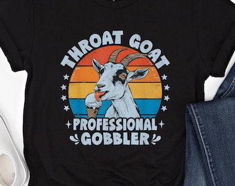 Puede incluir: Camiseta negra con un gráfico retro de una cabra comiendo un cono de helado. El texto "Throat Goat Professional Gobbler" está impreso en la camiseta.